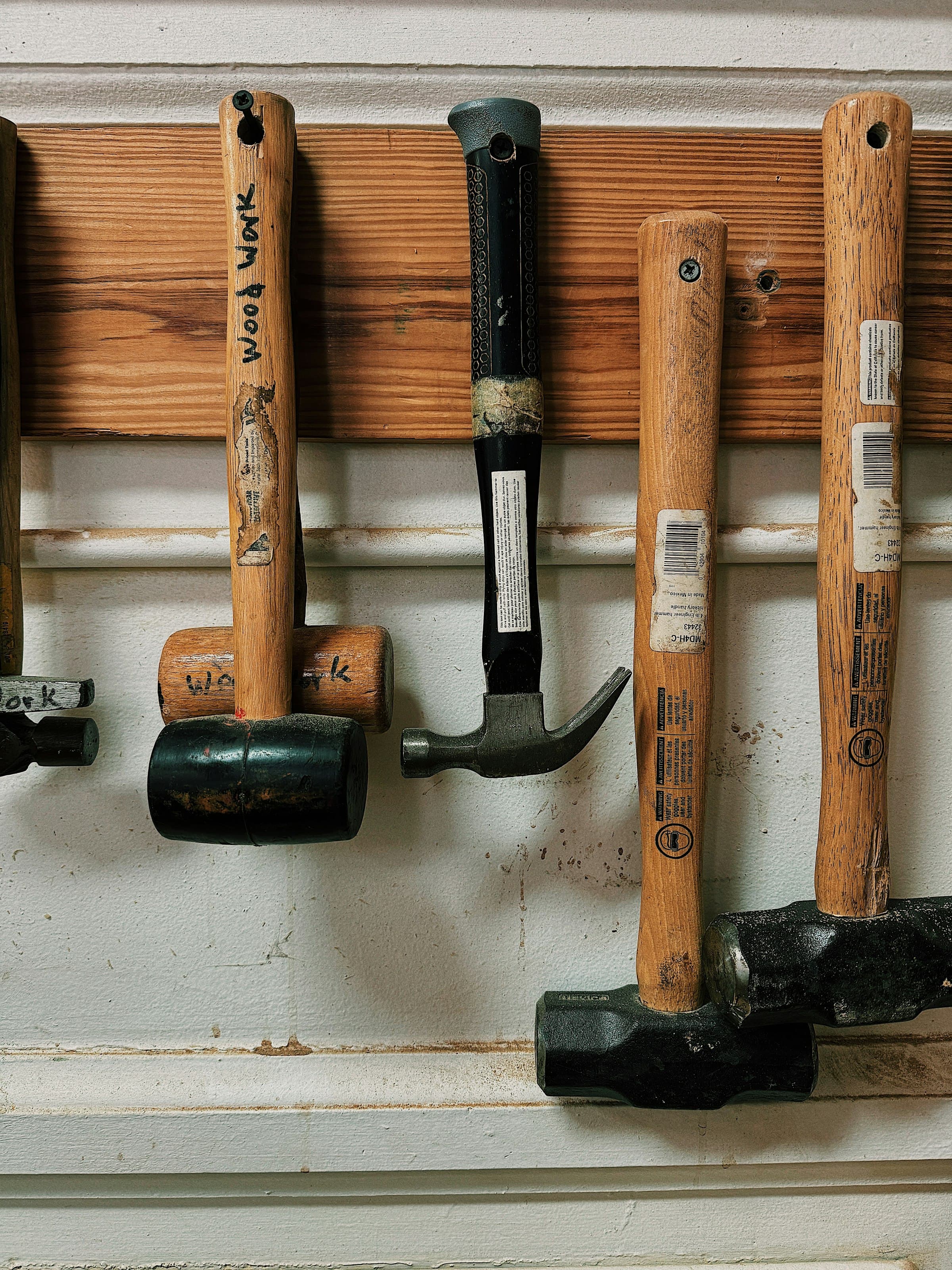 A row of hammers of varying sizes and shapes hanging on a workshop wall, from small tack hammers up to heavy mallets.