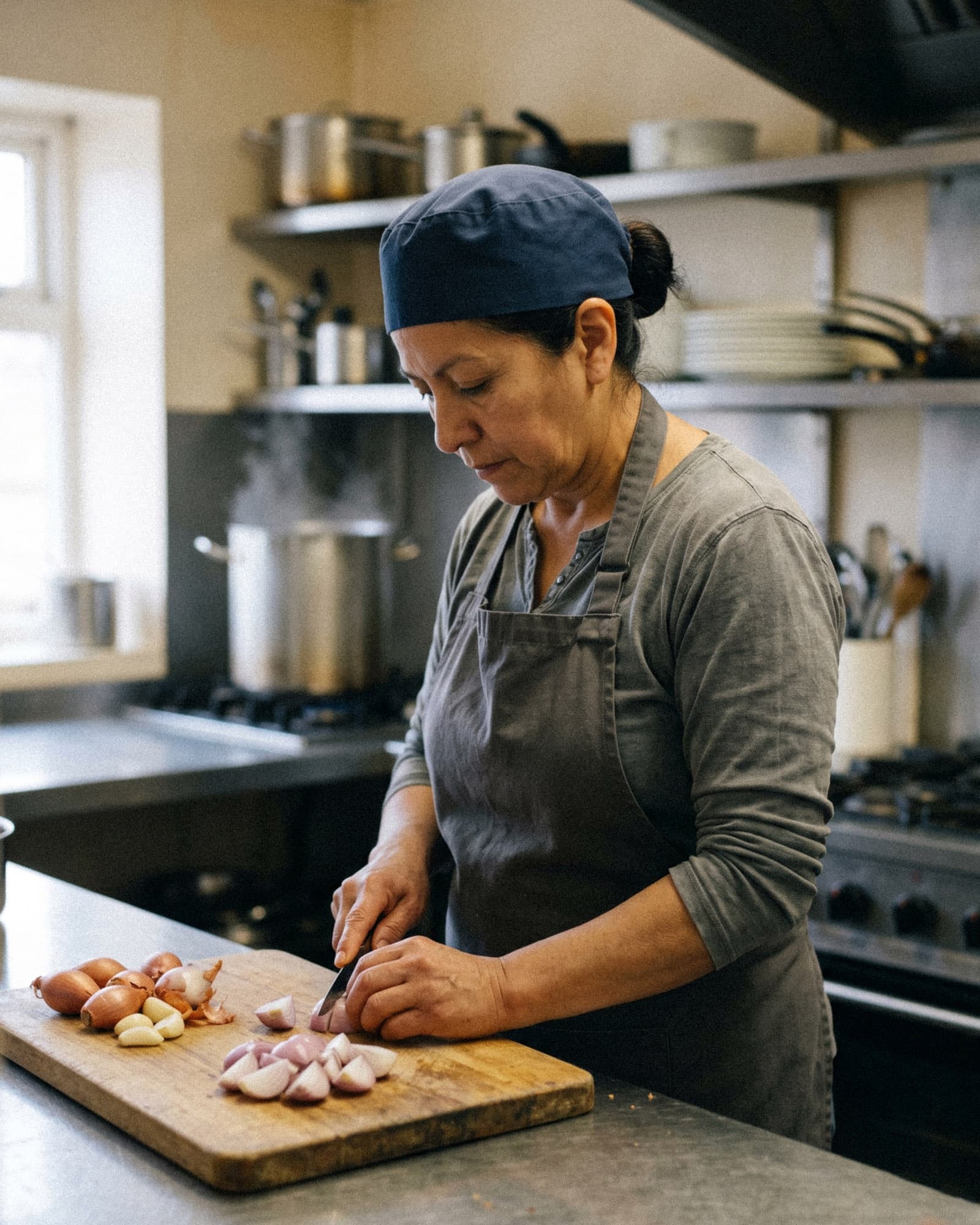 A cook quarters shallots on a wooden board in the prep kitchen of a small family pub.
