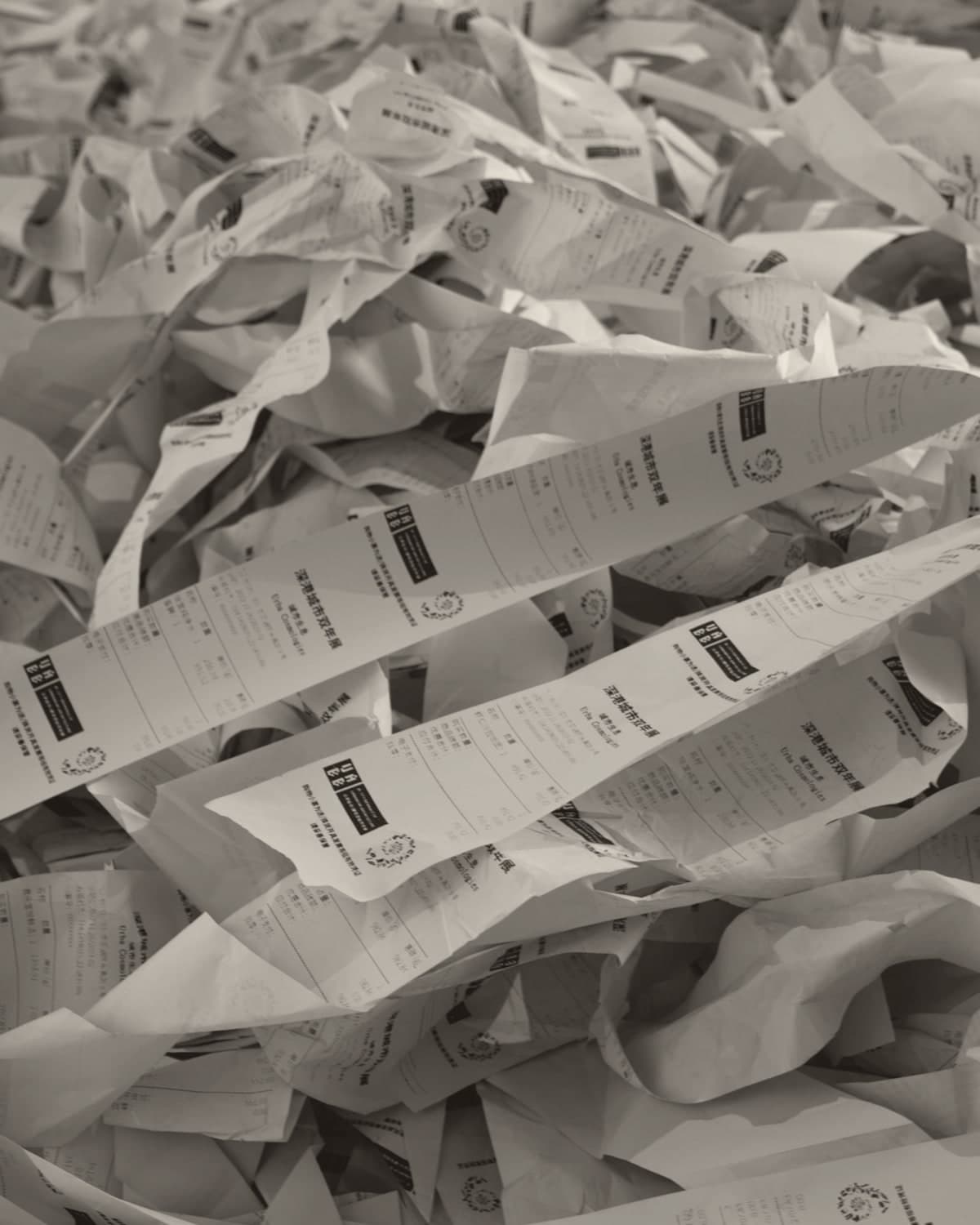 A deep pile of crumpled printed paper receipts, curled and overlapping so thickly that the floor beneath them disappears.