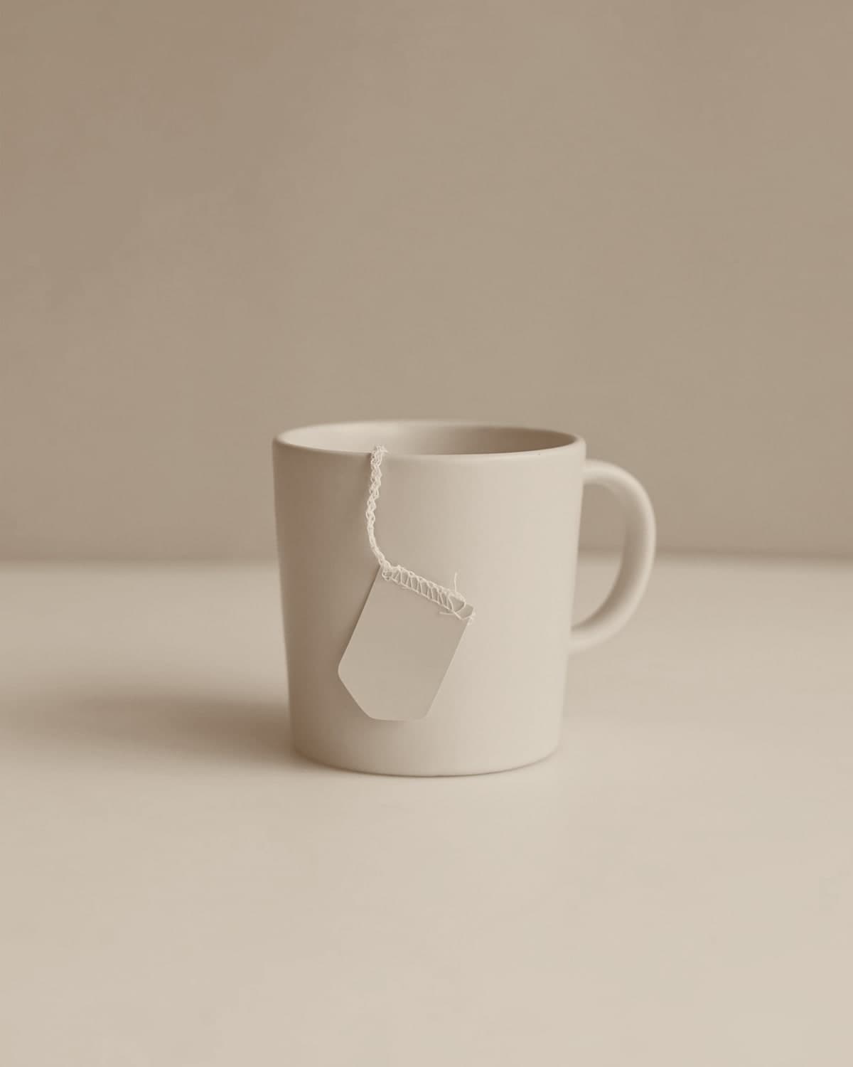 A pale blush ceramic mug set against a dusty blue backdrop, a yellow tea-bag tag hanging over the rim by its string, soft indirect light.