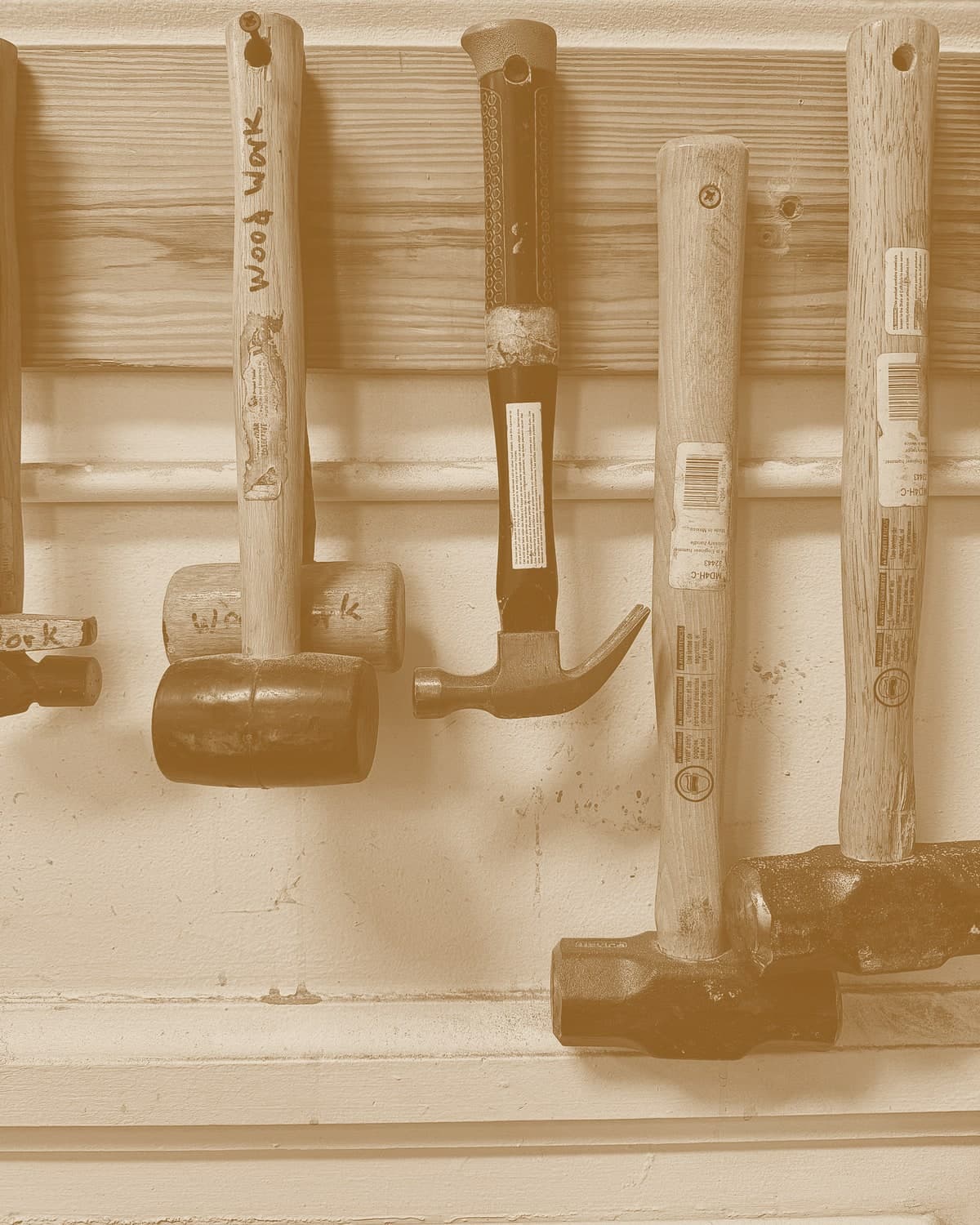 A row of hammers of varying sizes and shapes hanging on a workshop wall, from small tack hammers up to heavy mallets.