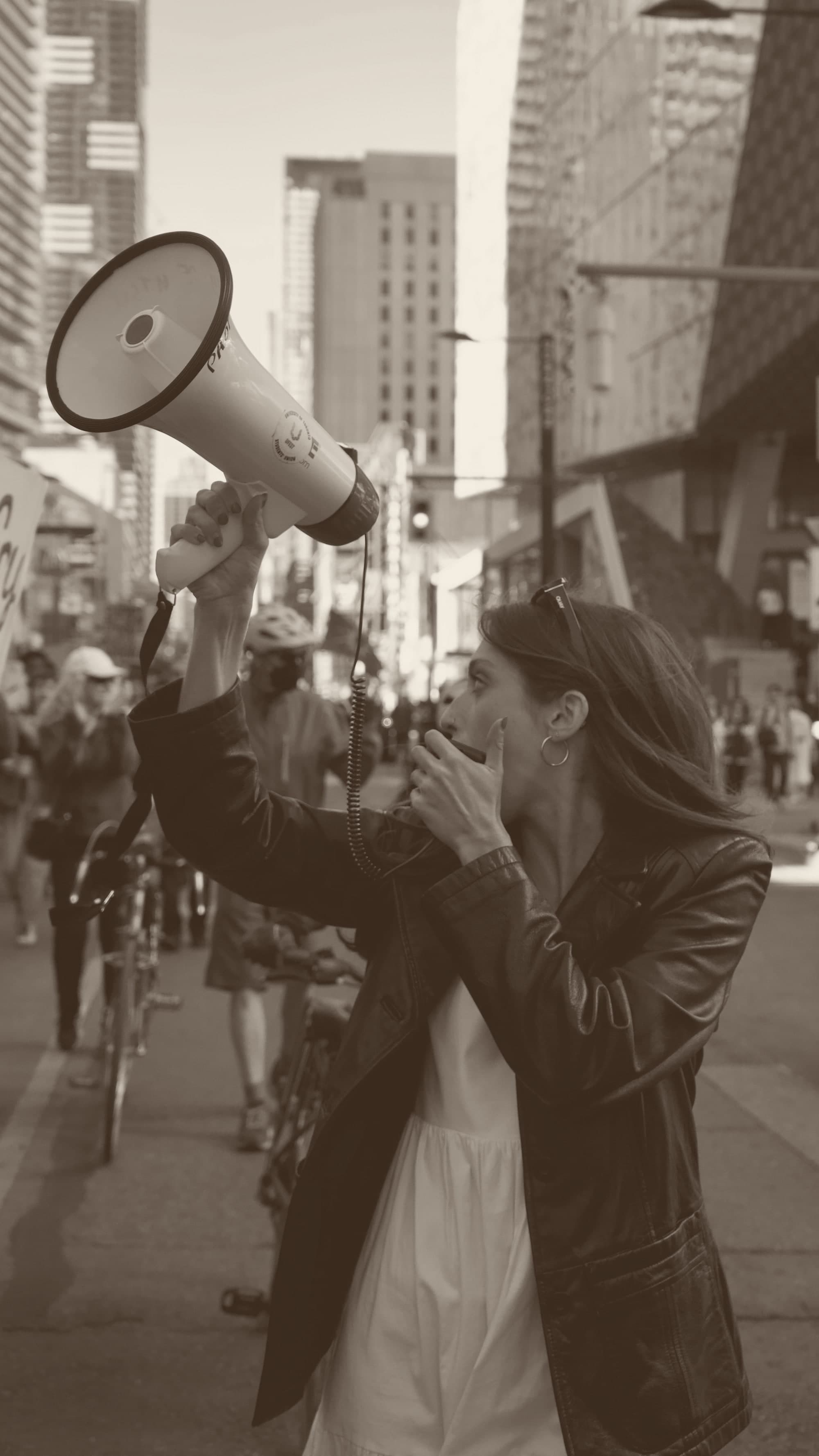 A person on a city street raising a megaphone and shouting into it.