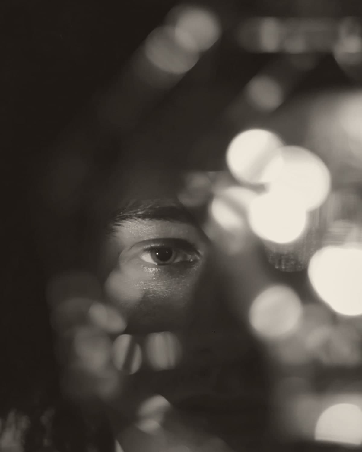 A single eye lit in teal by a handheld light, the rest of the face in shadow, warm bokeh lights blurring across the right half of the frame.