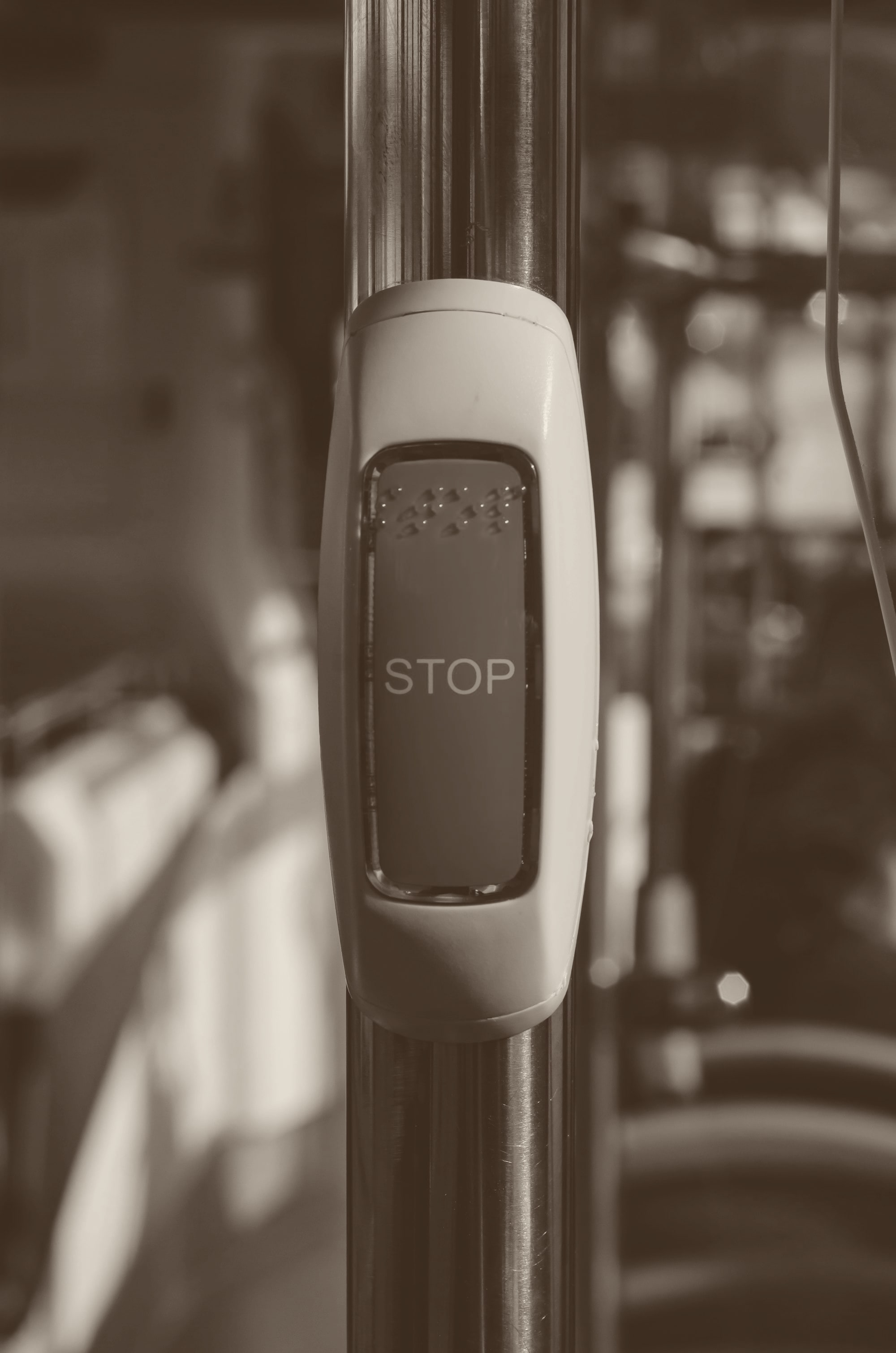 A red STOP button on the grab pole of a bus, lit by warm side light.