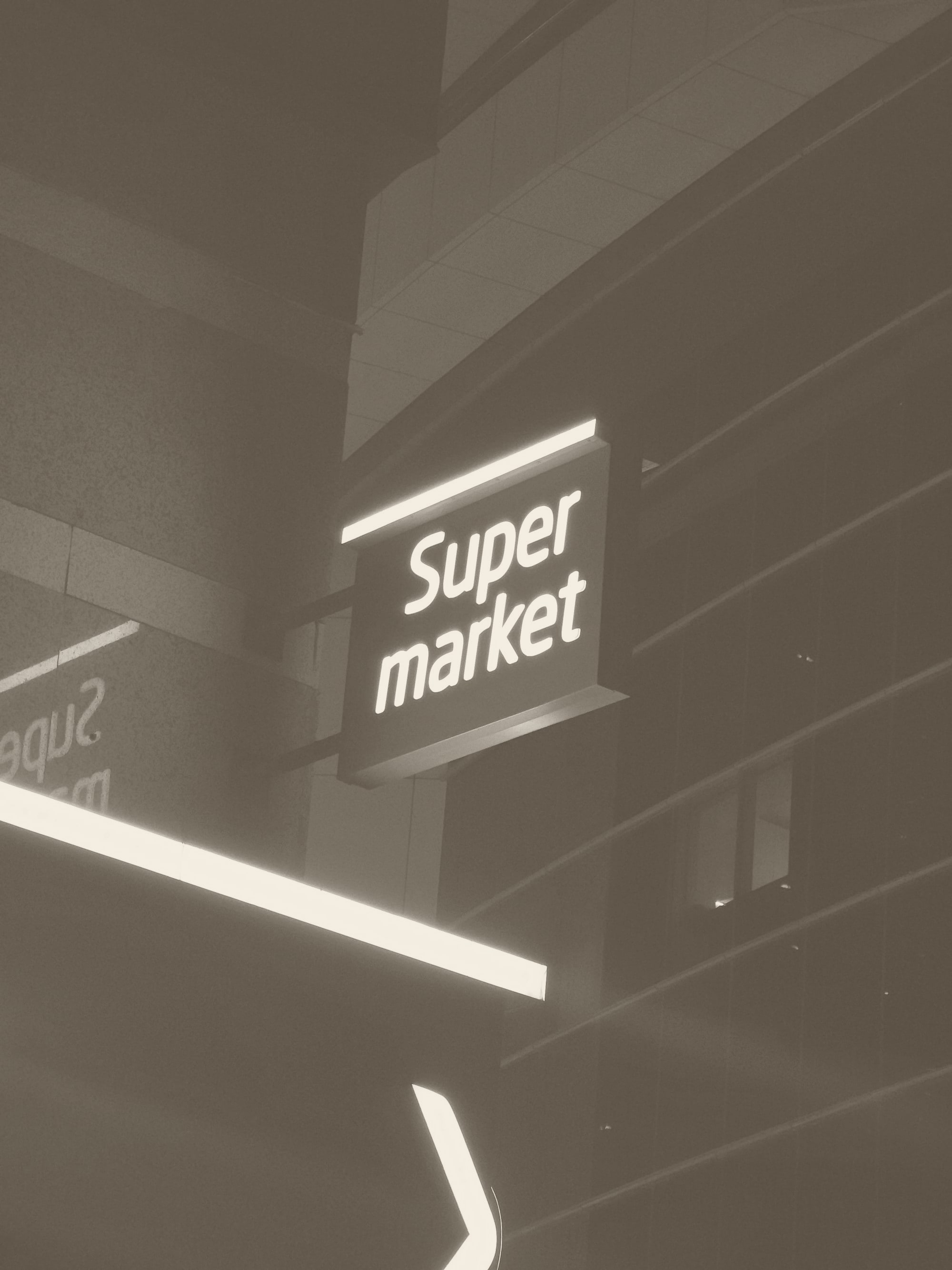 A neon sign that reads super market hanging from the side of a building.