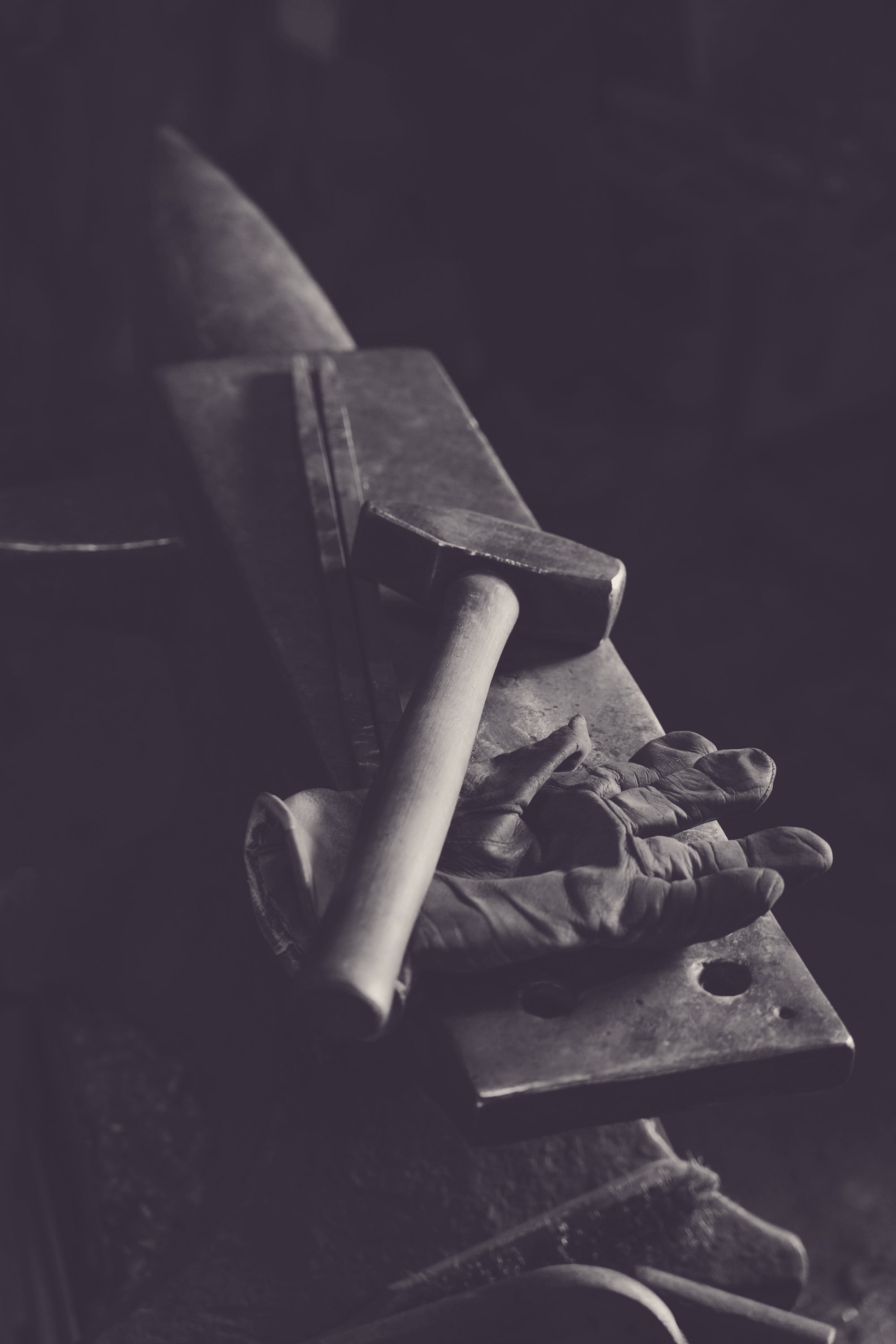 A blacksmith at the forge, hammer raised over glowing metal, sparks lifting from the anvil.